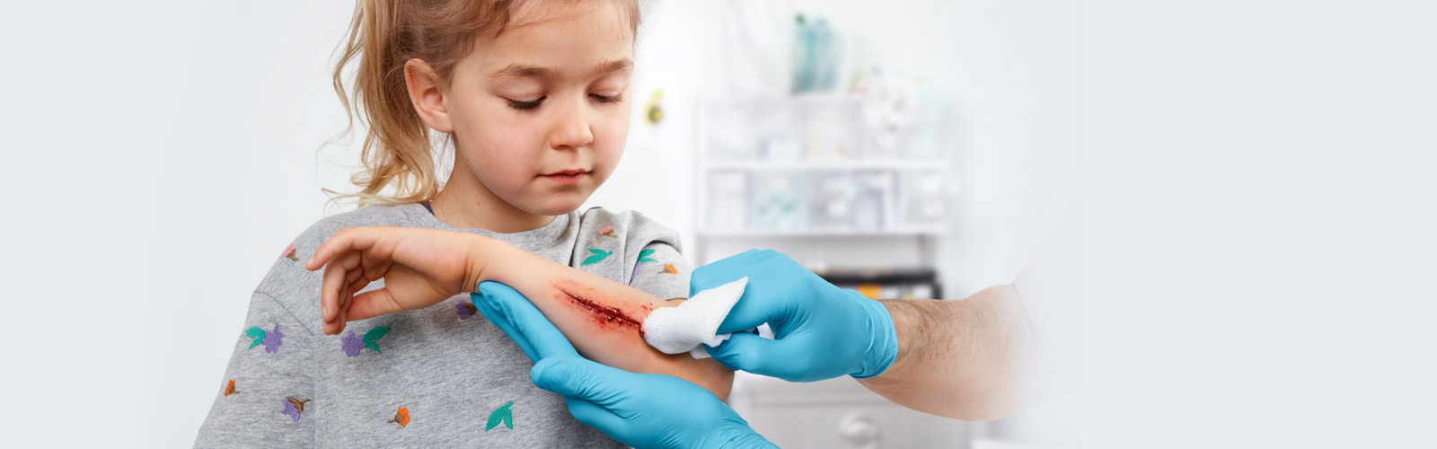 A young girl with an open wound on her forearm is getting the wound cleaned by a doctor. A young girl with an open wound on her forearm is getting the wound cleaned by a doctor.